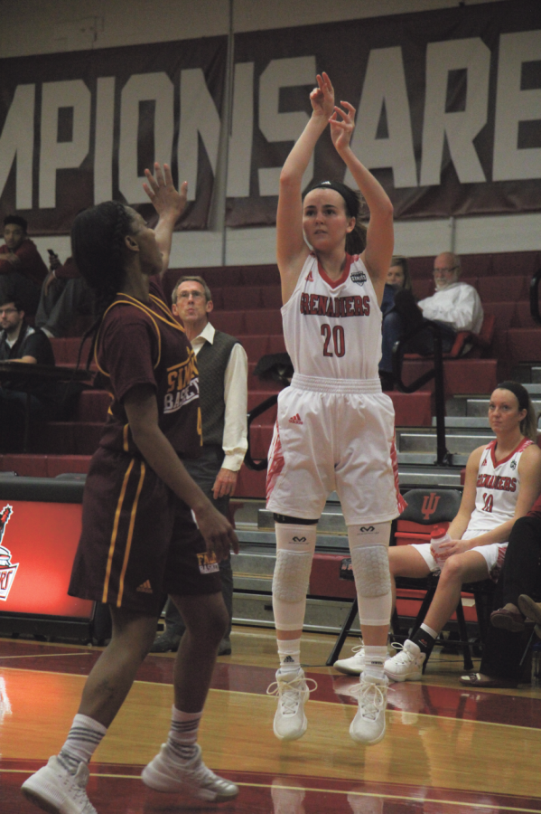 Madi Woods, sophomore guard, takes a three-point shot over her defender against Simmons College. 