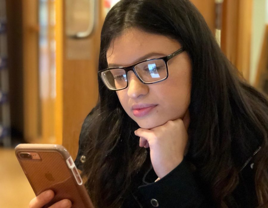 Angie Munoz, primary education sophomore, uses her phone during leisure time at University Grounds Coffee Shop. Photo by Meleena Richardson.