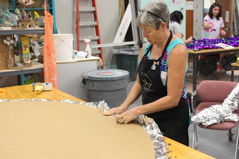 Donna Stallard, senior lecturer of Fine Arts, folds petal paper over the cardboard to make a giant silver circle for the Harvest Homecoming Float.