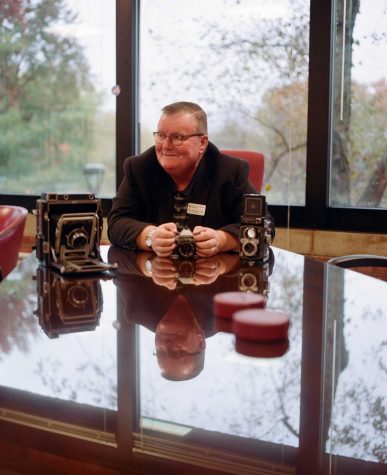 Former chancellor Ray Wallace sits in his office with some of his cameras.